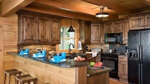 A wooden cabin-style kitchen with a central island, bar stools, and a black refrigerator. - Romantic Cabin,Views,Pet-Friendly,Trails (Ferguson)