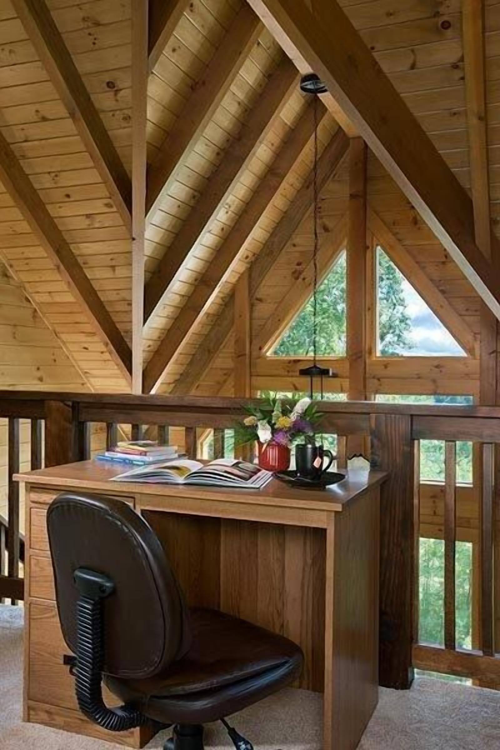 A wooden desk with a chair, a lamp, and a window with a view of trees.