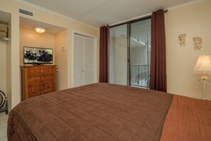 A bedroom with a large bed, a dresser, a television, a sliding glass door, and a lamp.