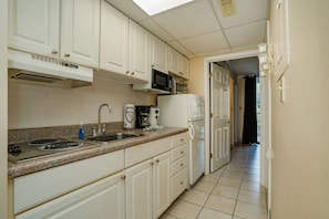 A kitchen with white cabinets, a microwave, a stove, a sink, and a refrigerator. - Oak Square 108 is a lovely condo with private balcony overlooks pool in downtown (Gatlinburg)