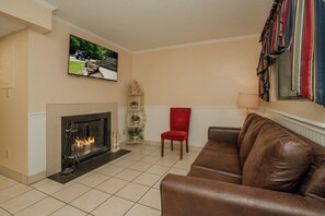 A living room with a fireplace, a red chair, a brown leather sofa, and a television mounted on the wall.