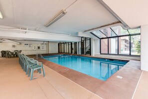Ein Innenpool mit großen Glaswänden, gefliestem Boden und einer Reihe von Stühlen an einer Seite.