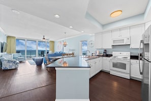A modern kitchen with white cabinets, a central island, and a view of the ocean. - Luxury Beachfront Condo w/ Pool & Sauna | Gulf Shores | Sleeps 10 (Gulf Shores)