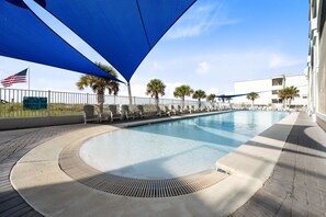 A swimming pool with a curved edge, surrounded by a paved walkway and shaded by a blue canopy.