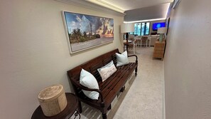 Un pasillo con un banco de madera, un cuadro y un televisor al fondo.