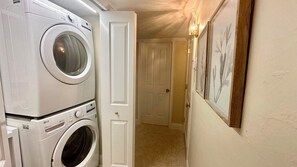A laundry room with stacked washers and dryers, a door leading to another room, and framed artwork on the wall. - Paradise Found at Atrium 203 Sanibel; 3br/3ba + Cabana (Sanibel)