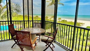 A balcony with a round table and four chairs, overlooking a beach and a pool.