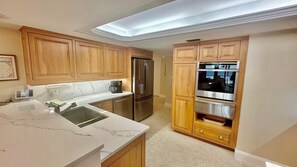 A modern kitchen with wooden cabinets, stainless steel appliances, and a marble countertop.