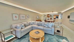 A modern living room with a sectional sofa, a round coffee table, and a dining area in the background. - Paradise Found at Atrium 203 Sanibel; 3br/3ba + Cabana (Sanibel)