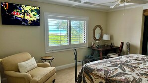 A bedroom with a bed, a chair, a desk, a mirror, and a window with blinds.