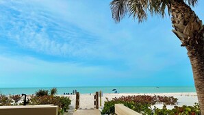 A wooden pathway leading to a beach with clear skies and calm waters.