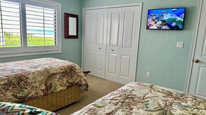A bedroom with two beds, a TV on the wall, and a window with blinds.