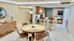 Un espace repas avec une table ronde et des chaises, un buffet et une cuisine en arrière-plan.