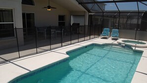 Una piscina exterior con cerramiento de vidrio, rodeada de sillas y un jacuzzi.
