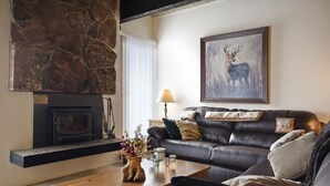 A cozy living room with a stone fireplace, a leather sofa, and a deer painting.