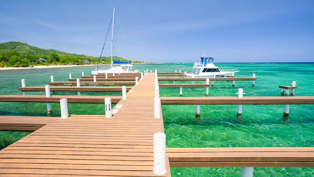 A wooden pier leading to a marina with boats docked, surrounded by clear turquoise water and a green landscape. - Pool, beach and sun- Parrot Fish 106 at Lawson Rock (Sandy Bay)