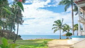 A beach view with palm trees, a sandy path, and a building with a balcony. - Pool, beach and sun- Parrot Fish 106 at Lawson Rock (Sandy Bay)