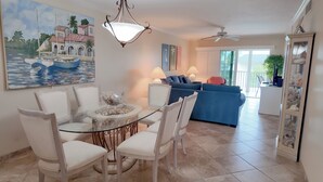 A dining area with a glass table surrounded by white chairs, a blue sofa in the background, and a ceiling fan. - 5 Star Rated (Sanibel)