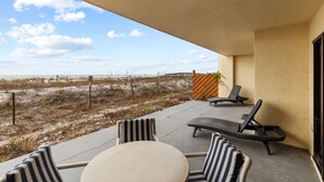 A covered outdoor seating area with a view of the beach, featuring lounge chairs and a table. - Surf Dweller 103 by Alicia Hollis Rental FREE ADVENTURES $300/Day (Fort Walton Beach)
