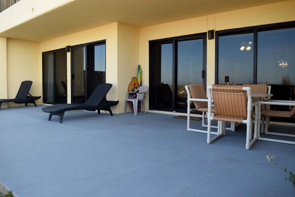 A covered outdoor area with lounge chairs and a table, large sliding glass doors, and a view of the sky.