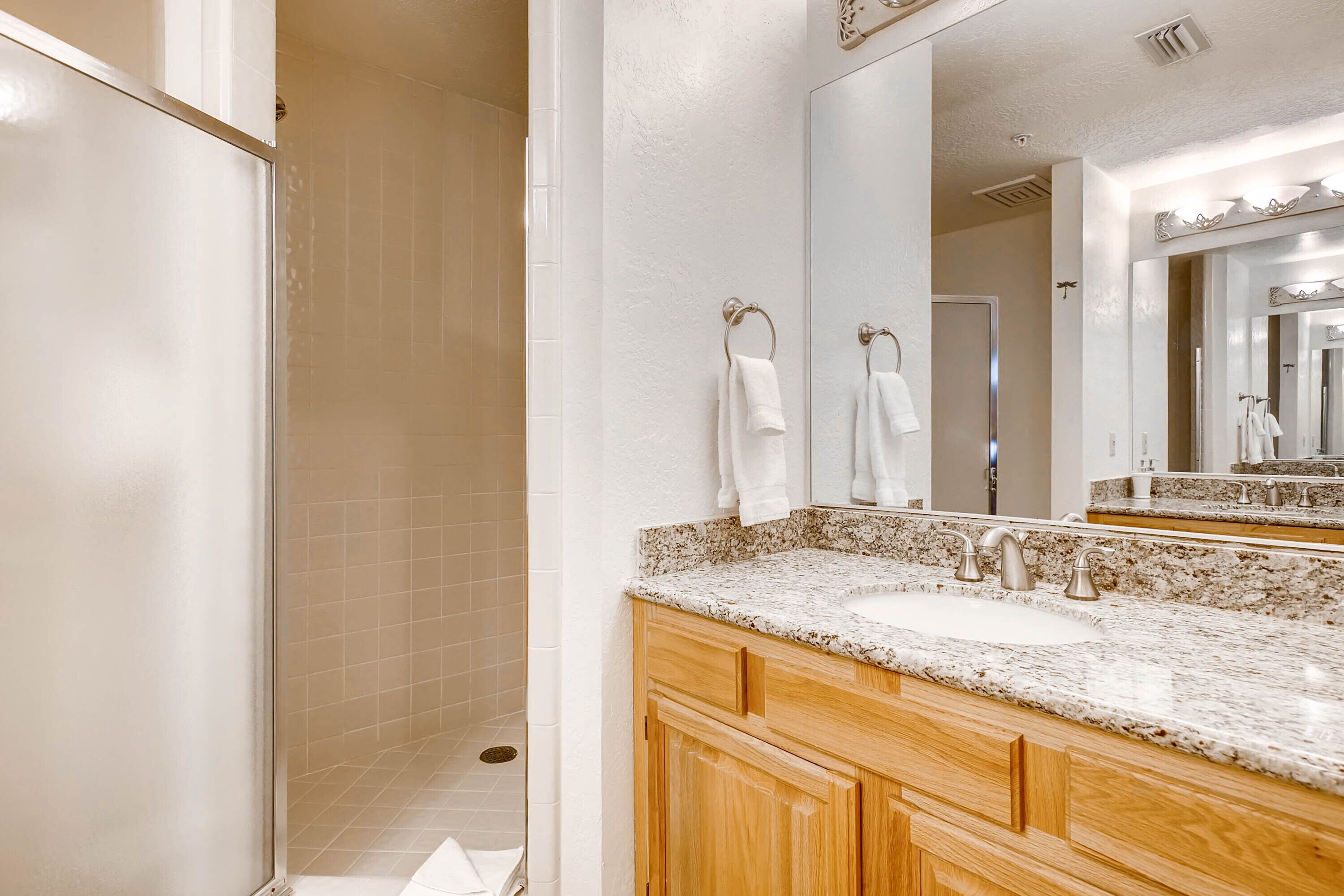 A bathroom with a white sink, wooden vanity, and a large mirror.