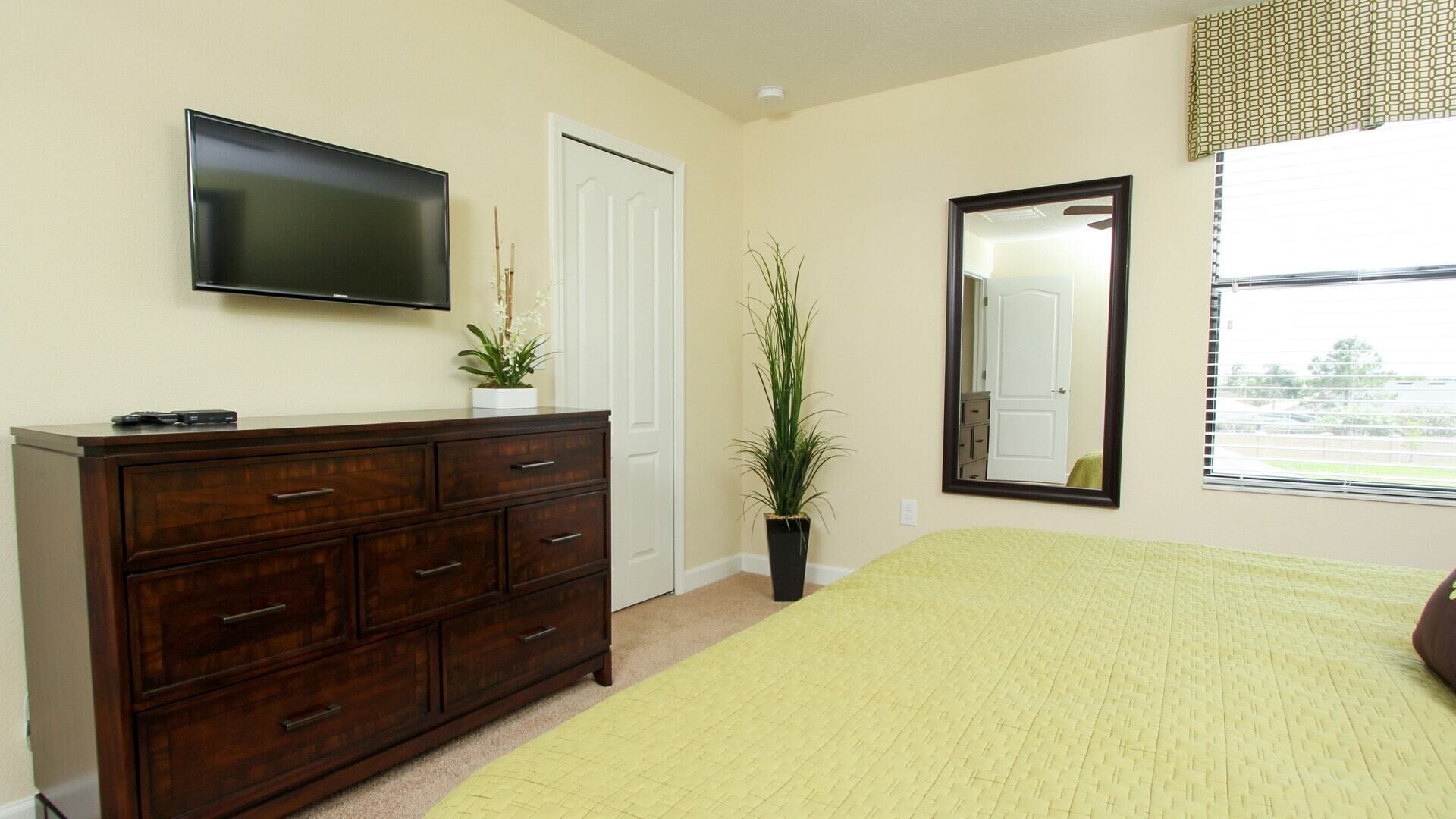 A bedroom with a bed, a dresser, a TV, a mirror, and a window.