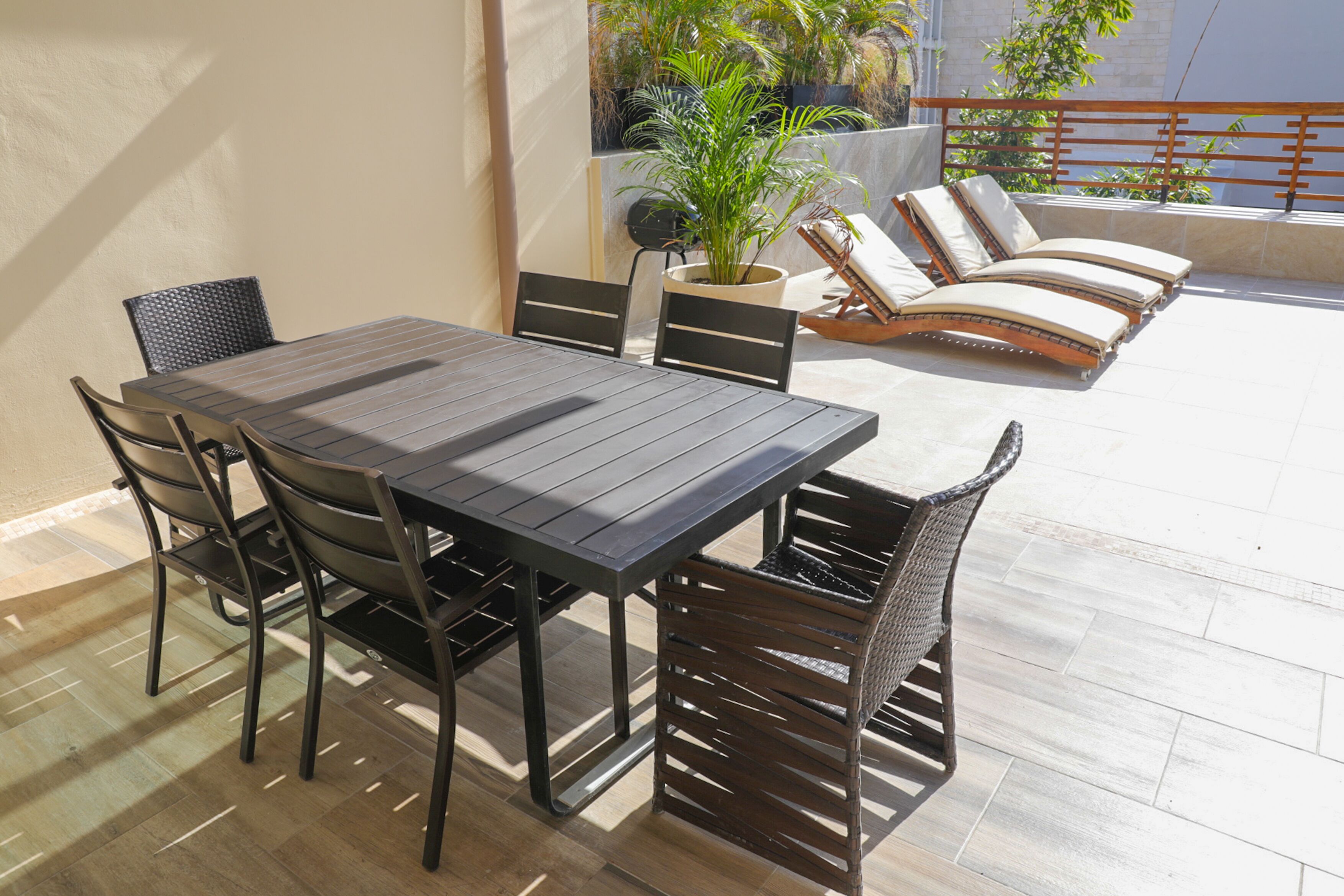Un patio al aire libre con una mesa y sillas de comedor, una planta en maceta y un área de estar con sillones.