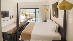 A hotel room with a large bed, a TV, a balcony with seating, and a view of the city.