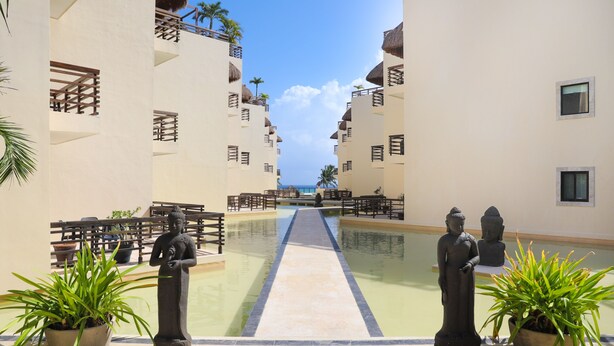 A resort pool area with a central water feature, potted plants, and a Buddha statue.