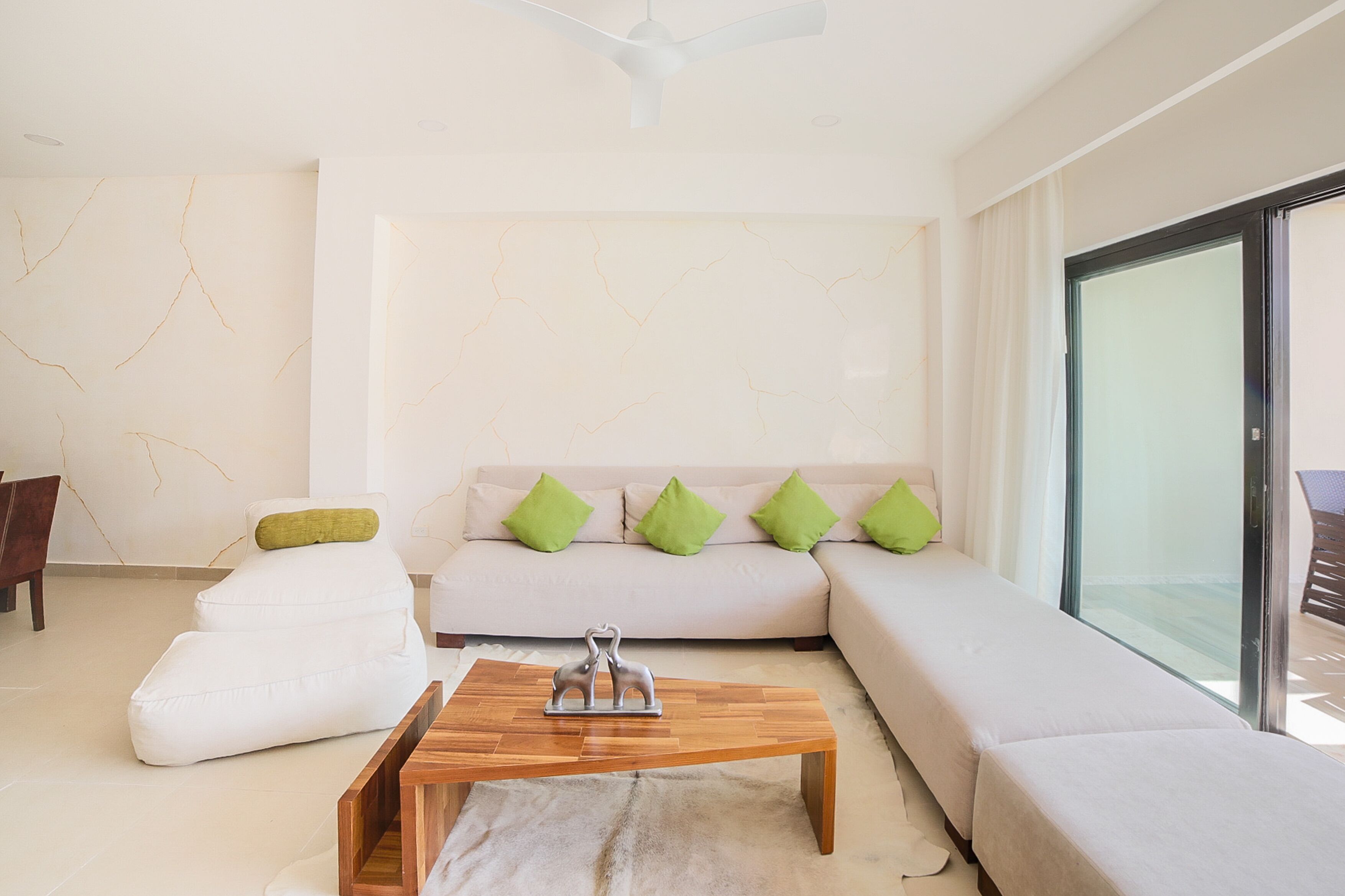 A modern living room with a sofa, a coffee table, and a glass door leading to an outdoor area.