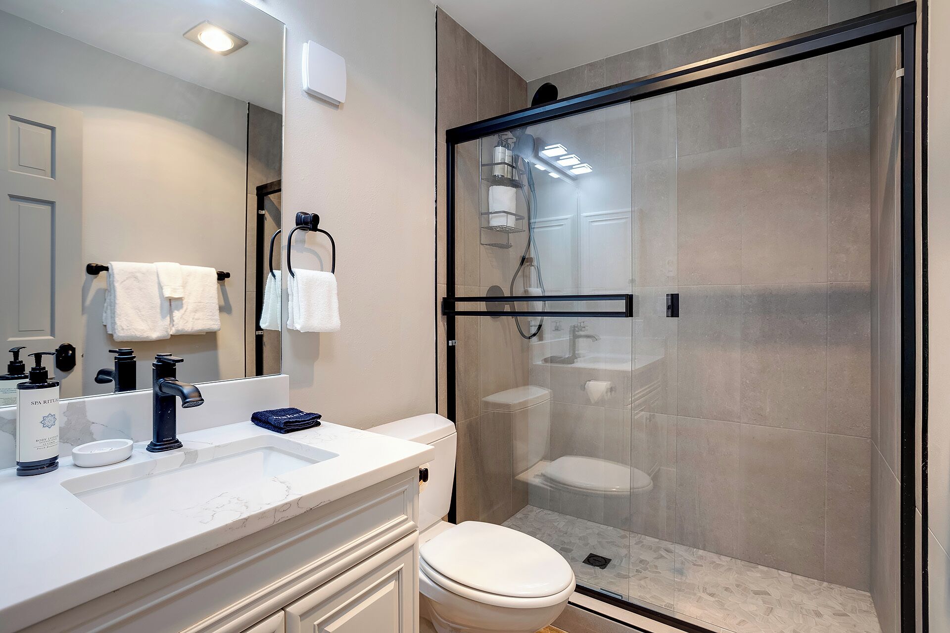 A modern bathroom with a glass-enclosed shower, a white toilet, and a marble sink.