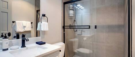 A modern bathroom with a glass-enclosed shower, a white toilet, and a marble sink.