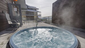 Ein Whirlpool auf einer Holzterrasse mit Blick auf ein Gebäude und einen bewölkten Himmel.