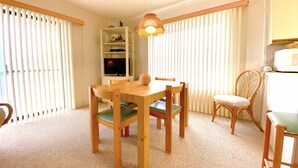 A dining area with a wooden table and chairs, a television on a shelf, and a hanging light fixture. - Ocean Princess 207-Oceanside 134th St, Elev, W/D, AC (Ocean City)