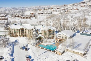 Un complejo turístico nevado con varios edificios, una piscina y montañas al fondo.