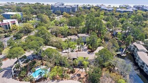 Vista aérea de uma área residencial costeira com vários edifícios, uma piscina e uma praia ao fundo.