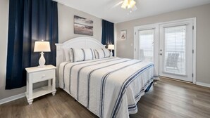 Une chambre à coucher comprenant un lit, des tables de chevet, un ventilateur de plafond et une porte avec des stores.