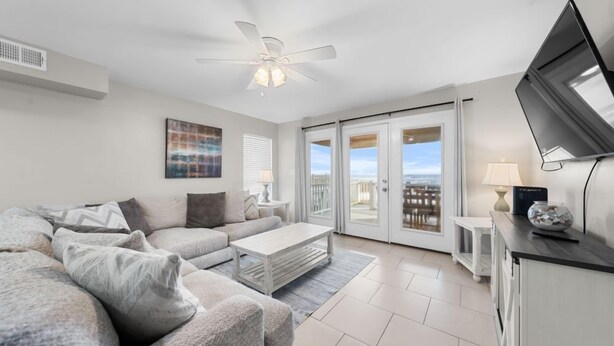 Un salon moderne avec un canapé, une table basse et un ventilateur de plafond. Une porte-fenêtre coulissante donne accès à un balcon avec vue.