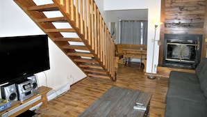 A living room with a wooden staircase, a fireplace, a television, and a sofa. - East Village Walk To Super Bee Lift Restaurants and Shops Hot Tub Access (Copper)