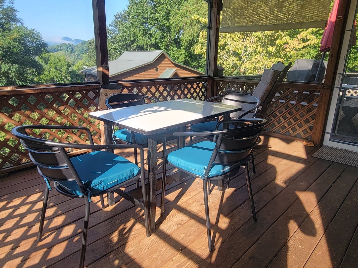 Une terrasse extérieure couverte, dotée d’une table et de chaises, qui offre une vue sur une zone boisée.