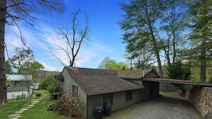 Une cabane rustique avec une allée en gravier, entourée d’arbres et d’un petit abri de jardin.