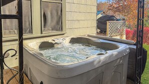 Un bain à remous installé à l’extérieur, avec une terrasse en bois et un barbecue en arrière-plan.
