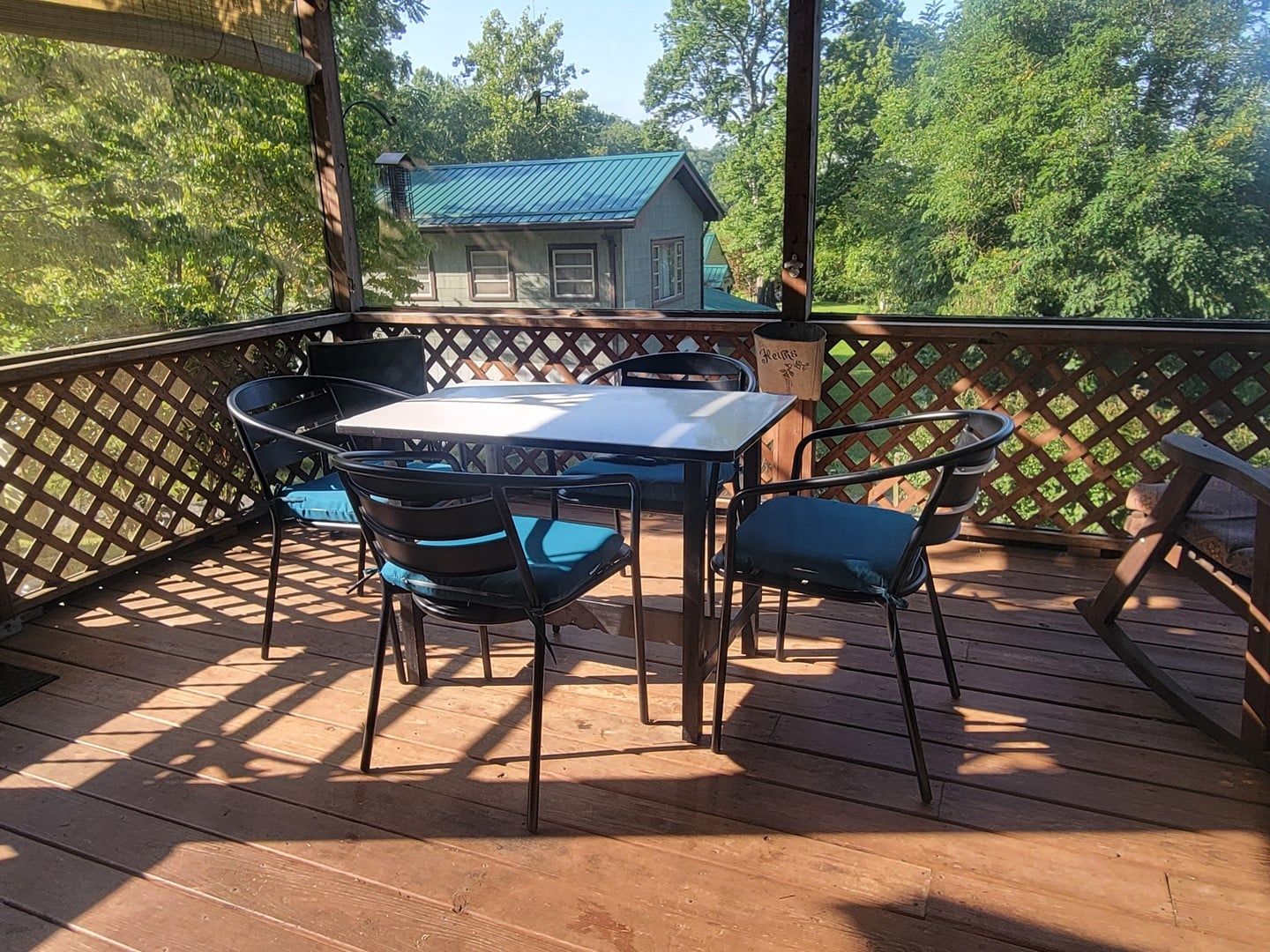 A wooden deck with a table and chairs, a view of a house with a blue roof, and a wooden fence.