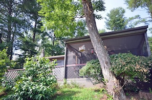 A residential property with a screened porch, a wooden fence, and a variety of greenery.
