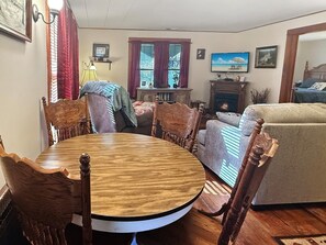 A dining area with a round wooden table and four chairs, a fireplace, a television, and a sofa in a living room. - Valley View Cottage - Quiet Cabin w/Firepit near Deep Creek and downtown + free railroad tix (Bryson City)