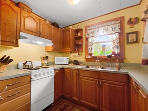 A kitchen with wooden cabinets, a white stove, a microwave, and a window with curtains. - Valley View Cottage - Quiet Cabin w/Firepit near Deep Creek and downtown + free railroad tix (Bryson City)