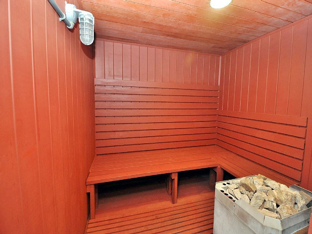 Una sauna con paredes y bancos de madera, un calentador y un recipiente lleno de piedras.