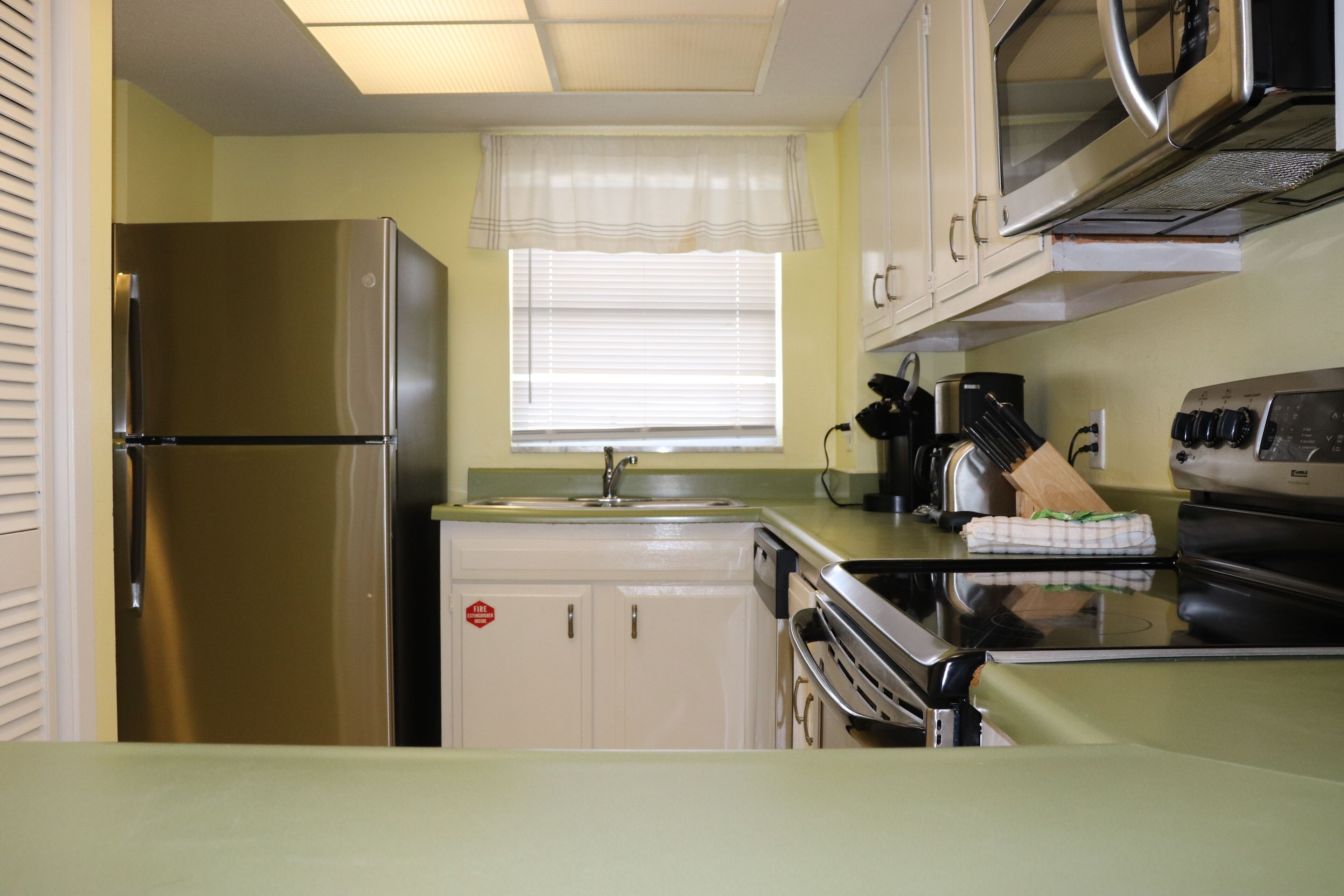 A compact kitchen with a stainless steel refrigerator, a microwave, an oven, and a sink.