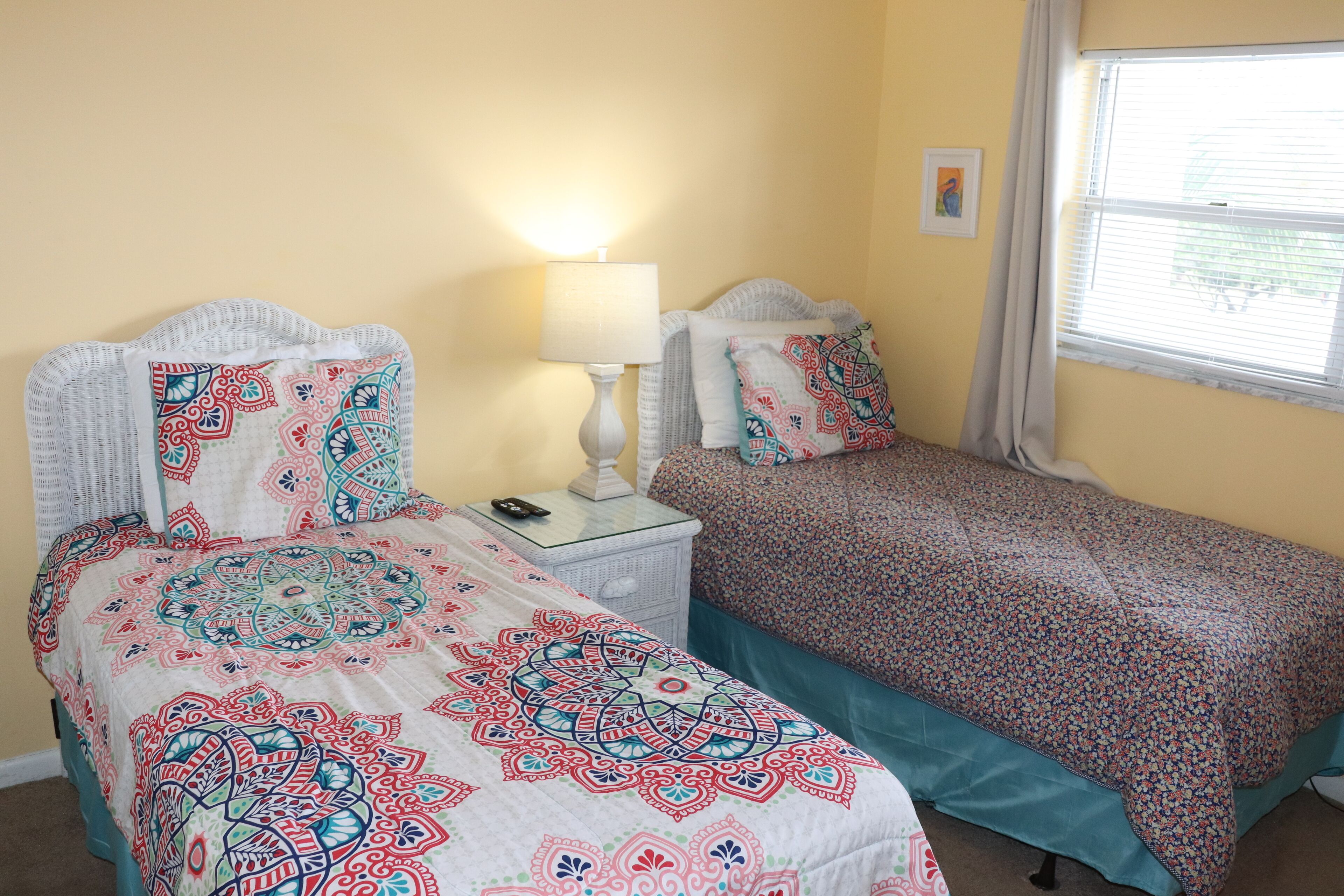 A bedroom with two beds, a nightstand, a lamp, and a window with blinds.