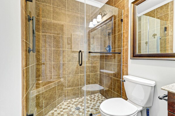 Een badkamer met een douchecabine van glas, een toilet en een wastafel.